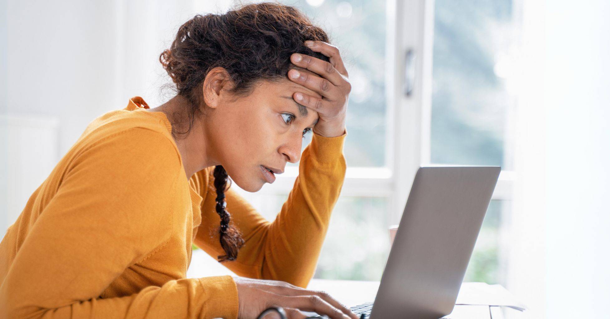 women sitting leaning looking atlaptop with hand on her forehead in disbelief